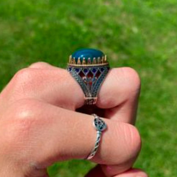 Hand wearing a decorative ring with a blue gemstone against a green background