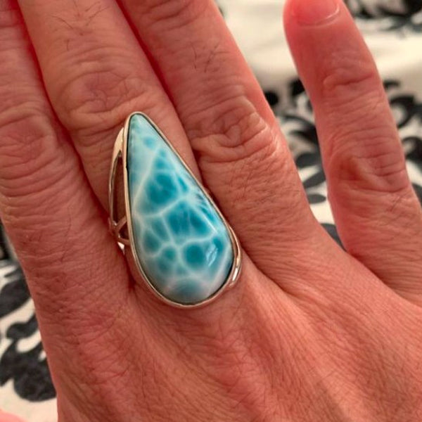 Larimar ring on a person's finger with a patterned background