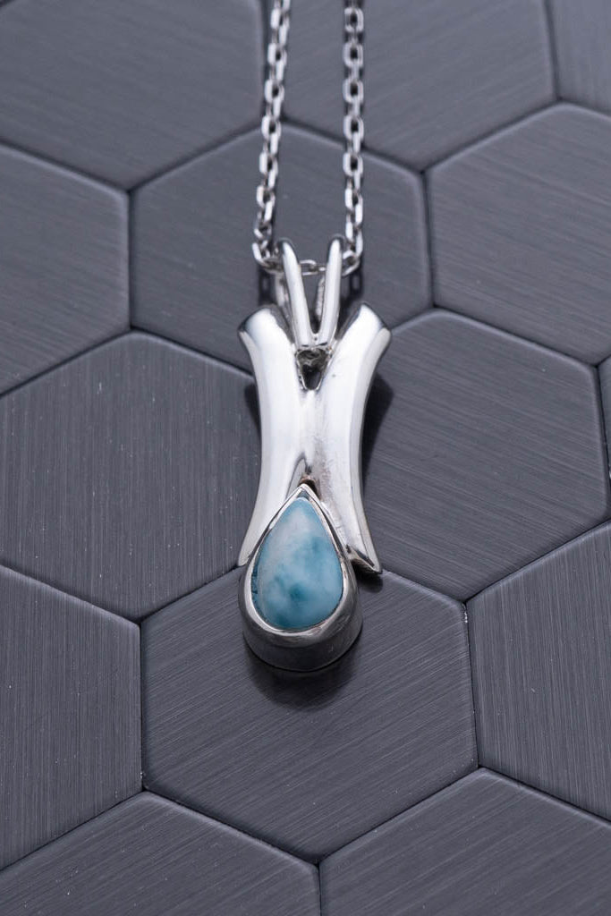 Silver pendant with a blue gemstone on a hexagonal patterned surface