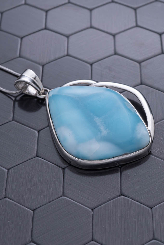 Turquoise pendant on a silver chain against a hexagonal patterned background