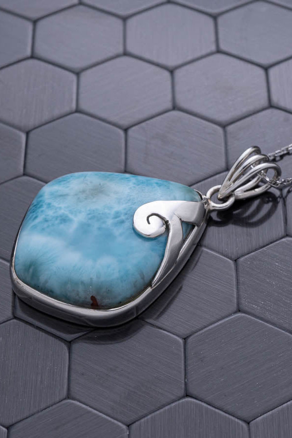 Turquoise stone pendant with silver wave design on a hexagonal patterned surface