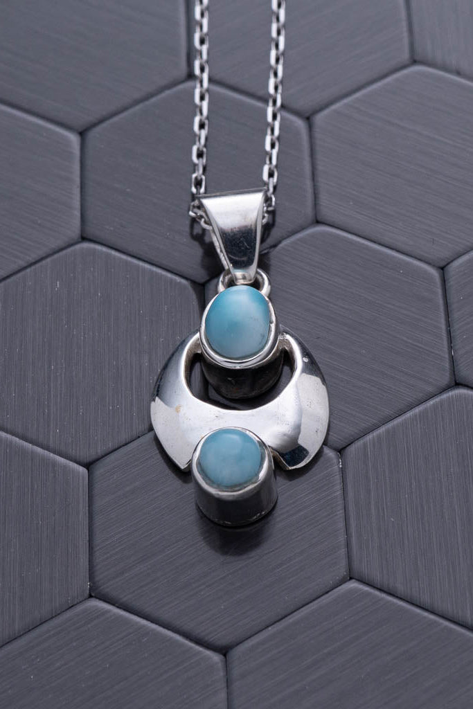 Silver pendant with turquoise stones on a hexagonal patterned background