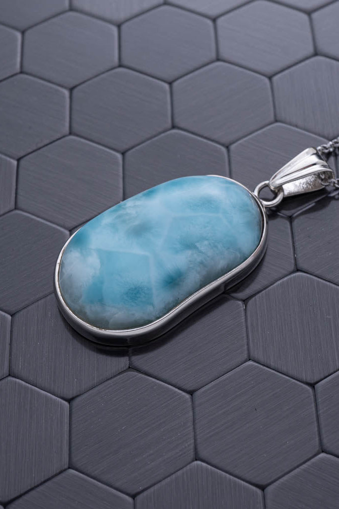 Turquoise stone pendant on a silver chain against a hexagonal patterned gray background
