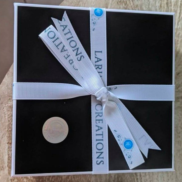 Black box with a white ribbon and circular object inside, featuring 'Larimar Creations' branding.