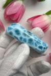 A freeform Larimar cabochon highlighting its unique blend of deep blue and turquoise tones, accented by natural white marbling patterns.
Pink Tulips background.