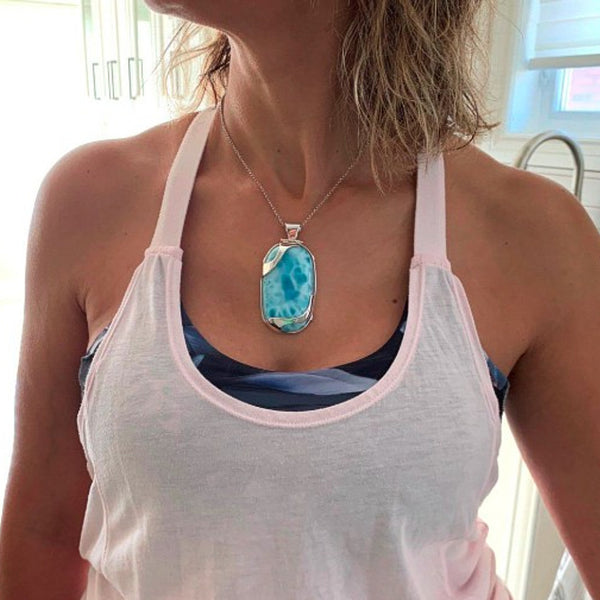 Person wearing a light pink tank top with a blue pendant necklace.