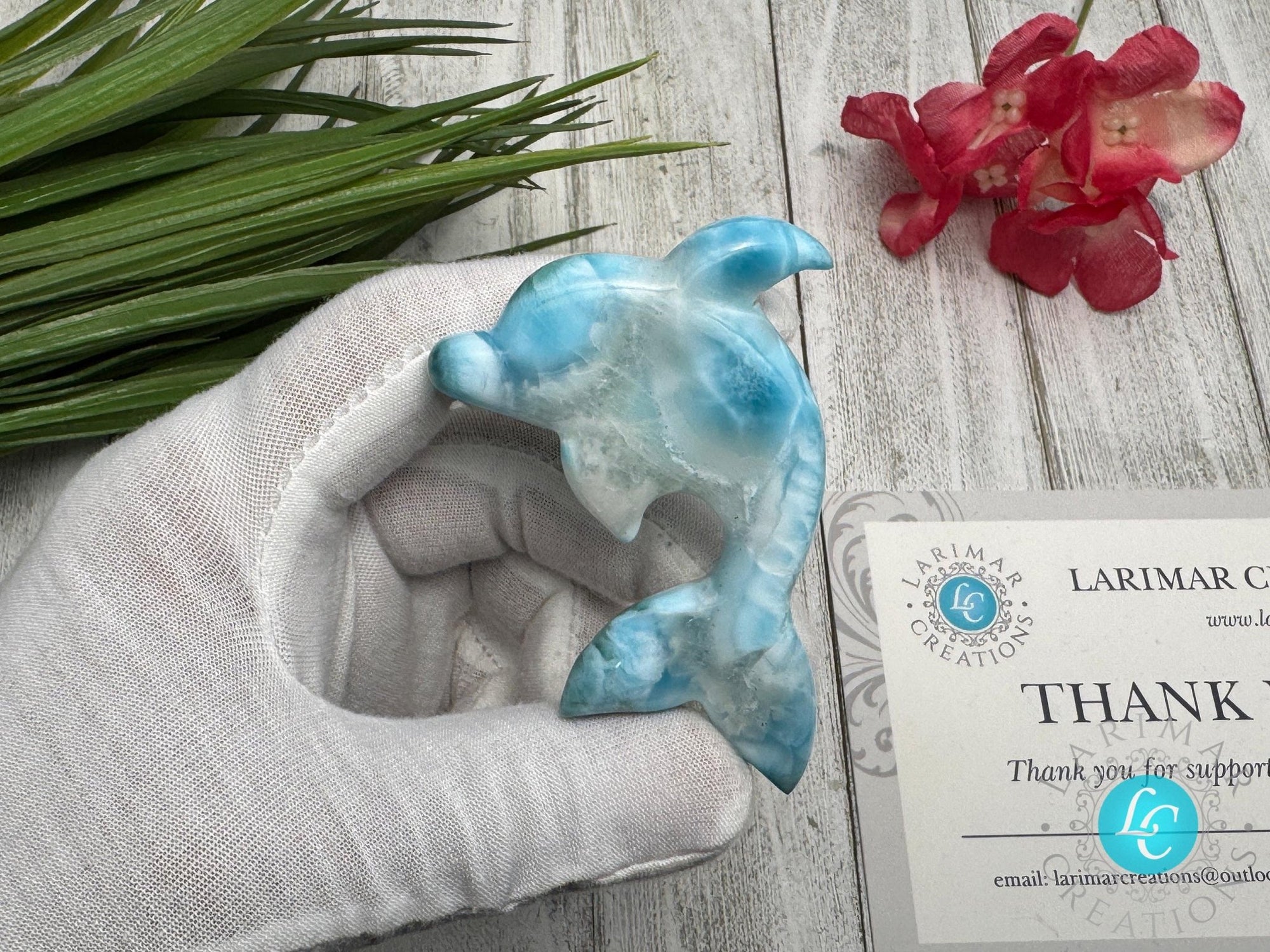 Hand holding a polished larimar dolphin carving with blue and white marbling, displayed on a light wooden surface with