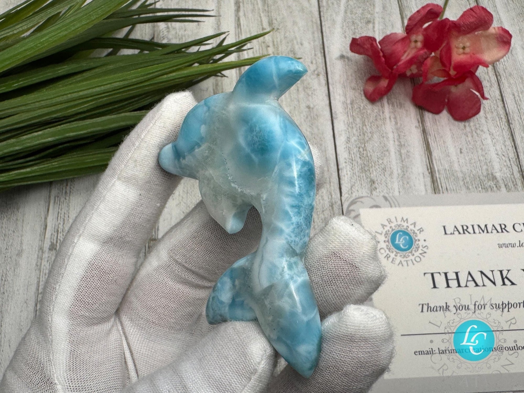 Hand holding a polished larimar dolphin carving with blue and white marbling, displayed on a light wooden surface with