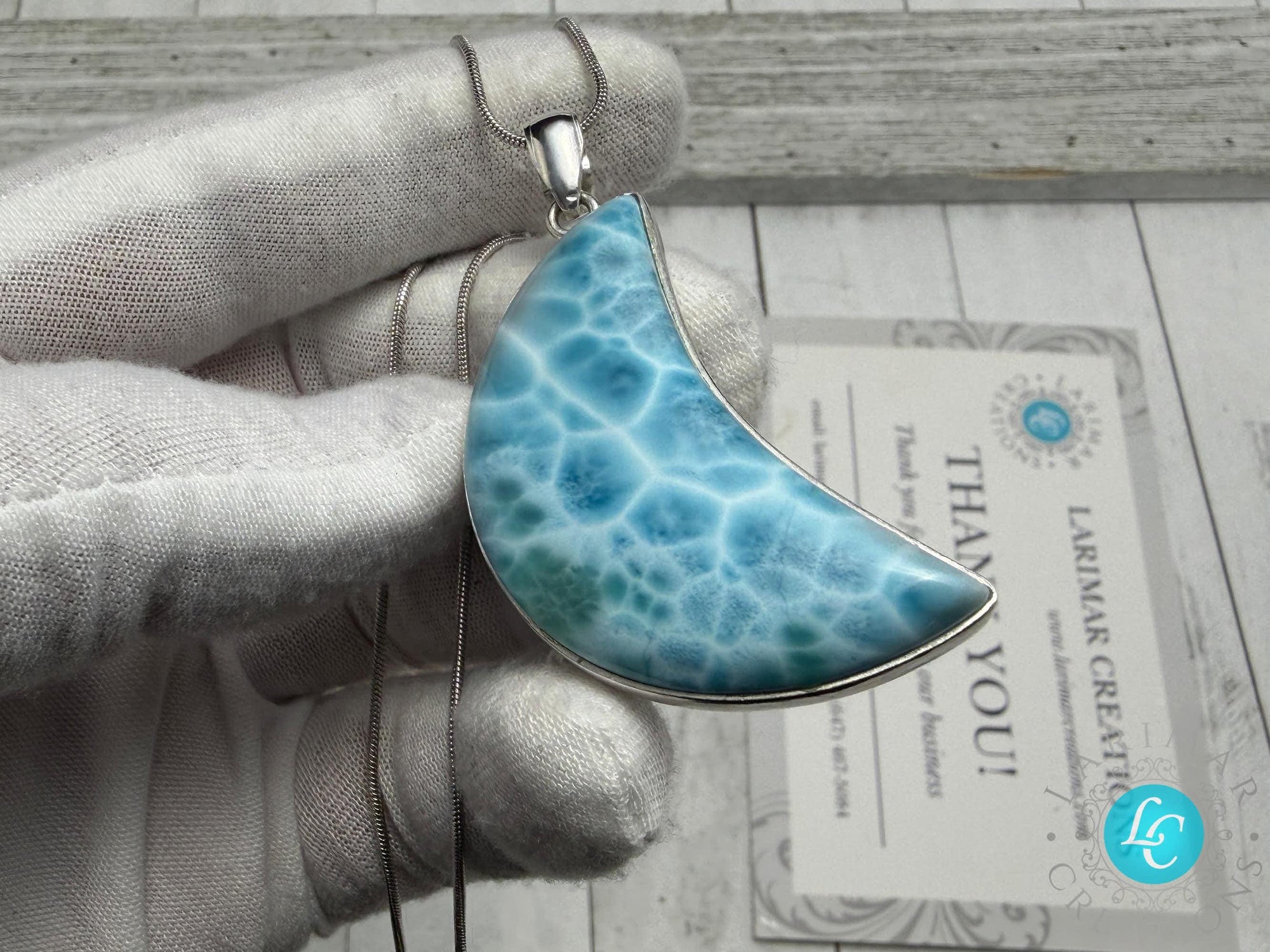 Larimar crescent moon pendant in sterling silver, featuring a natural blue Caribbean gemstone with ocean-wave patterns, held in a gloved hand.