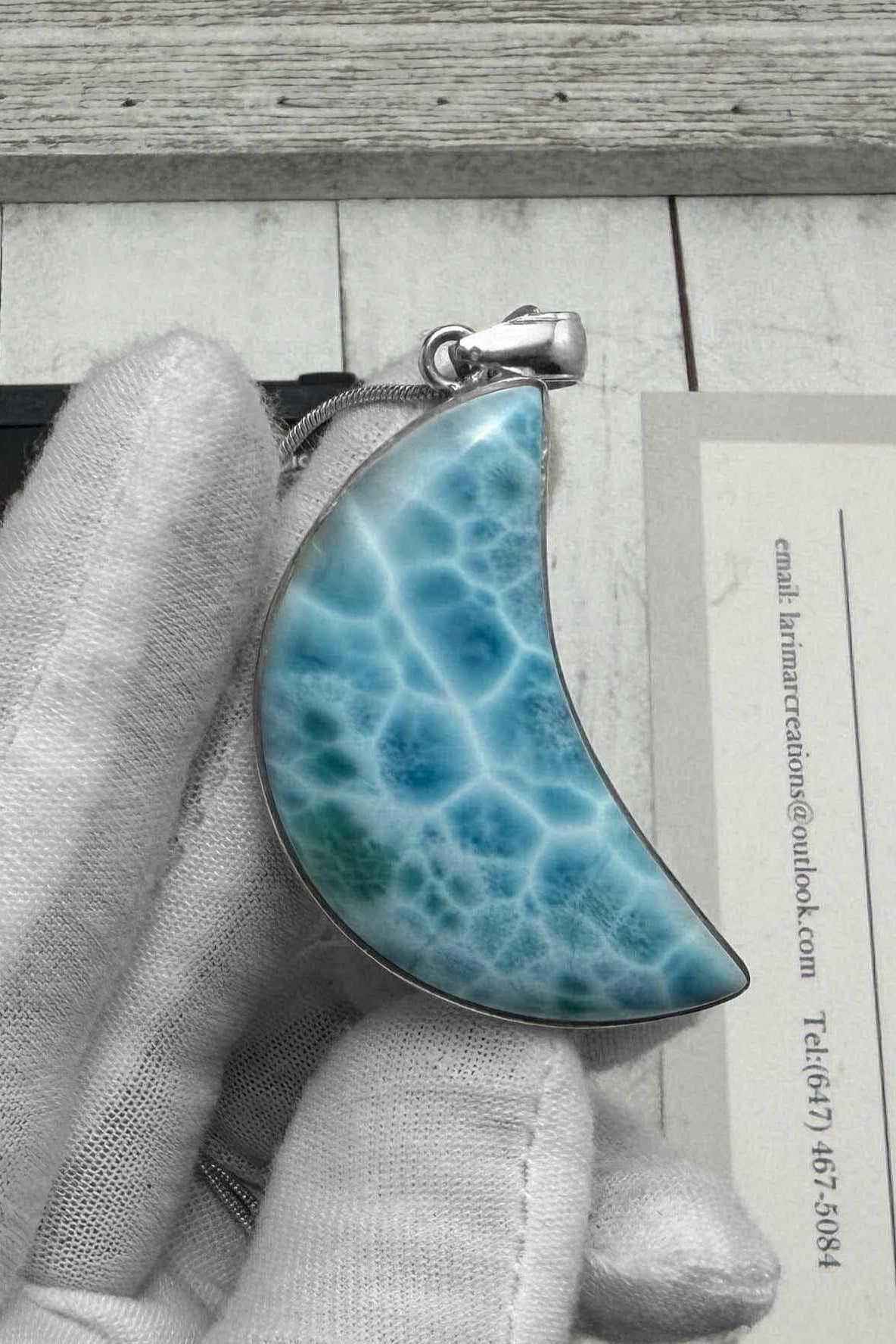 Larimar crescent moon pendant in sterling silver, featuring a natural blue Caribbean gemstone with ocean-wave patterns, held in a gloved hand.