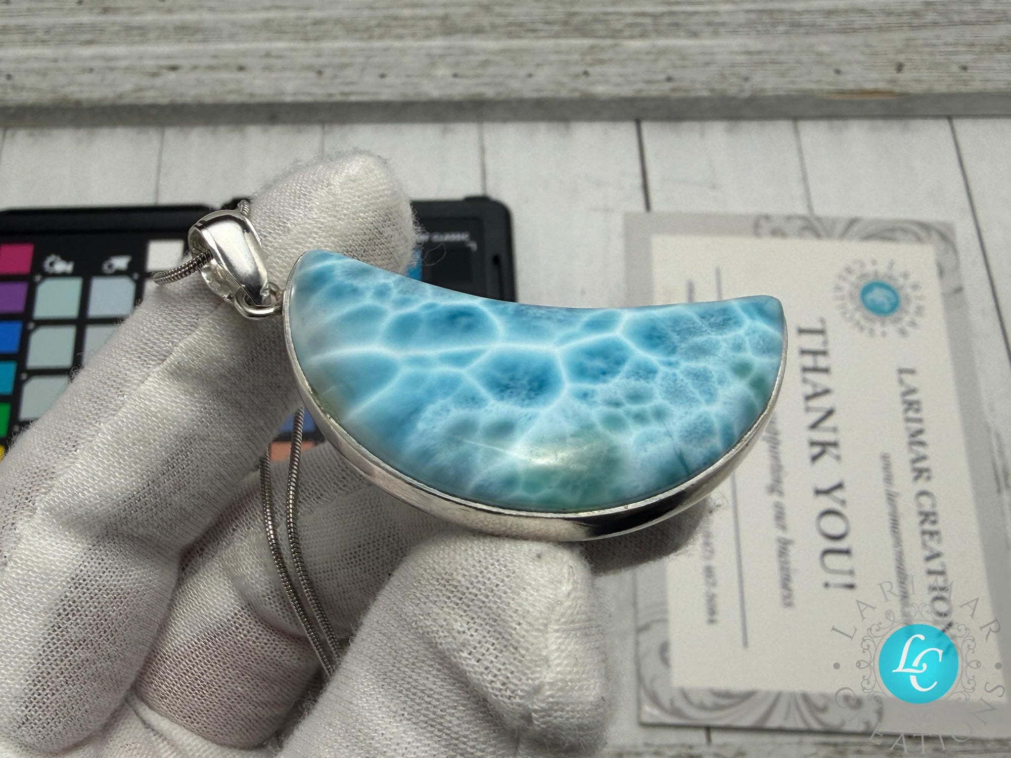Larimar crescent moon pendant in sterling silver, featuring a natural blue Caribbean gemstone with ocean-wave patterns, held in a gloved hand.