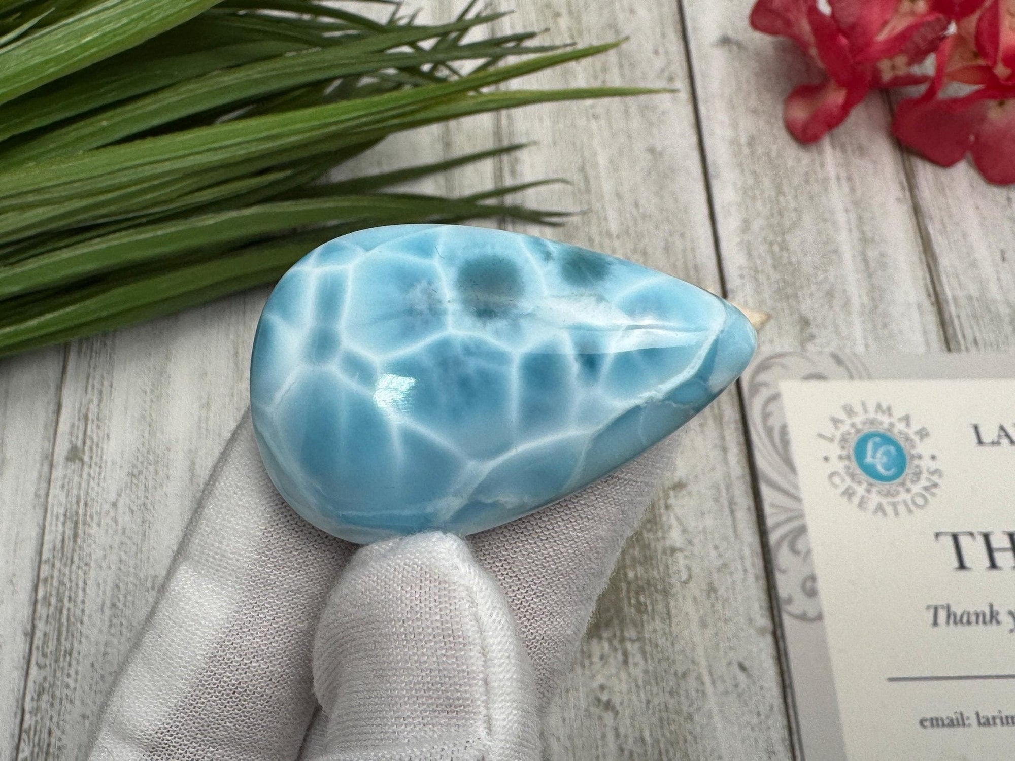 High-quality blue Larimar gemstone with ocean-like patterns, displayed in a white-gloved hand next to a branded
