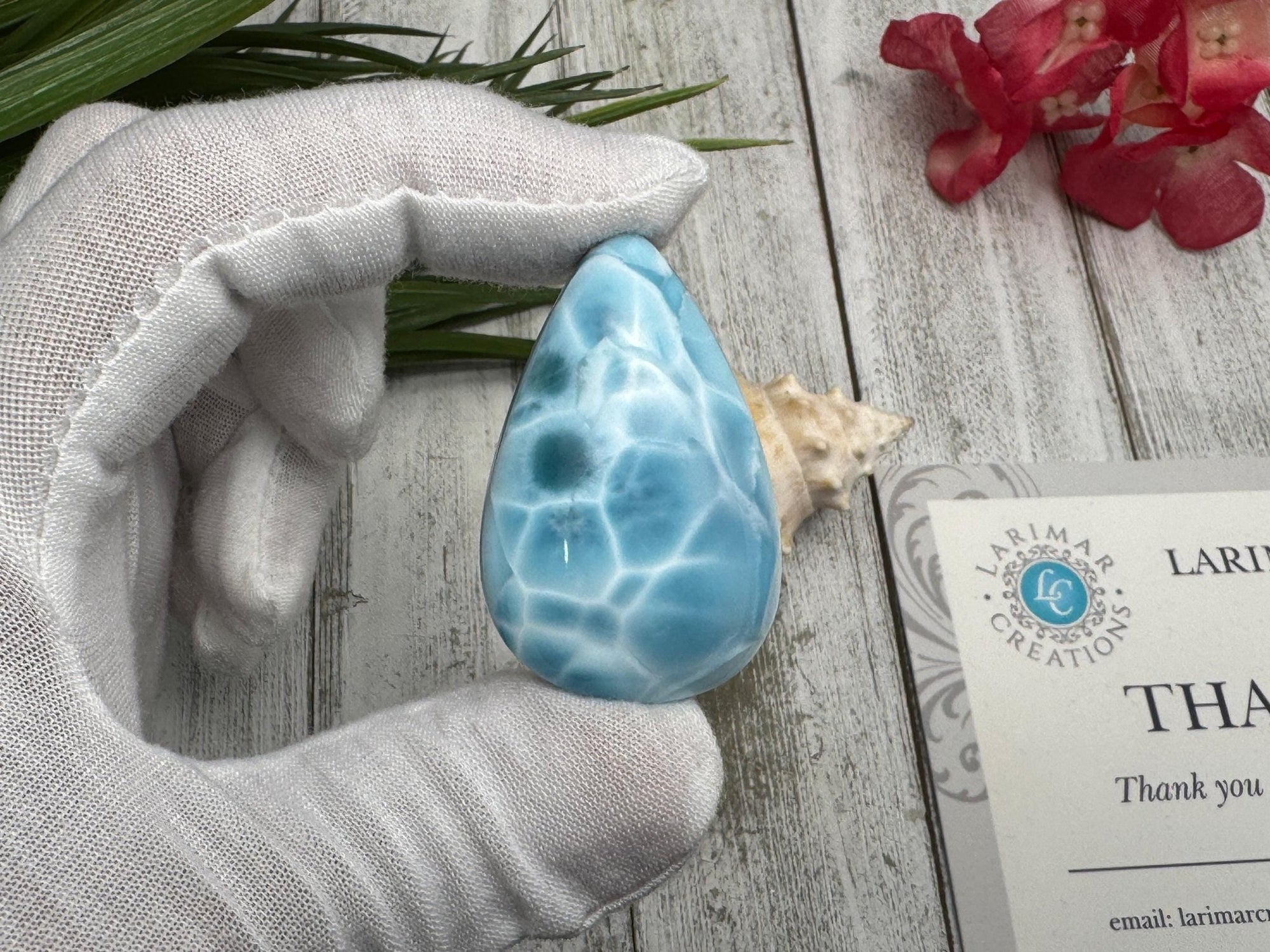 High-quality blue Larimar gemstone with ocean-like patterns, displayed in a white-gloved hand next to a branded