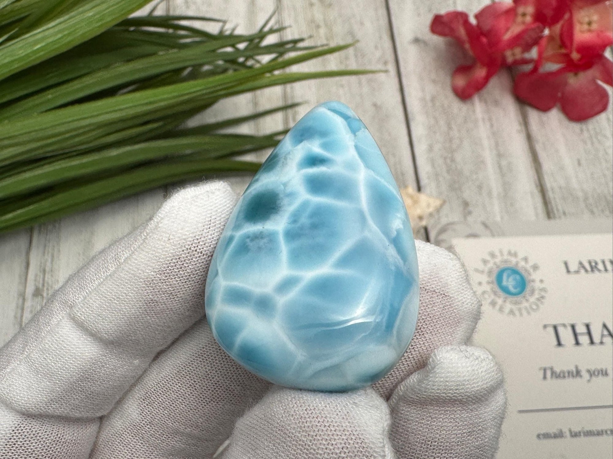 High-quality blue Larimar gemstone with ocean-like patterns, displayed in a white-gloved hand next to a branded