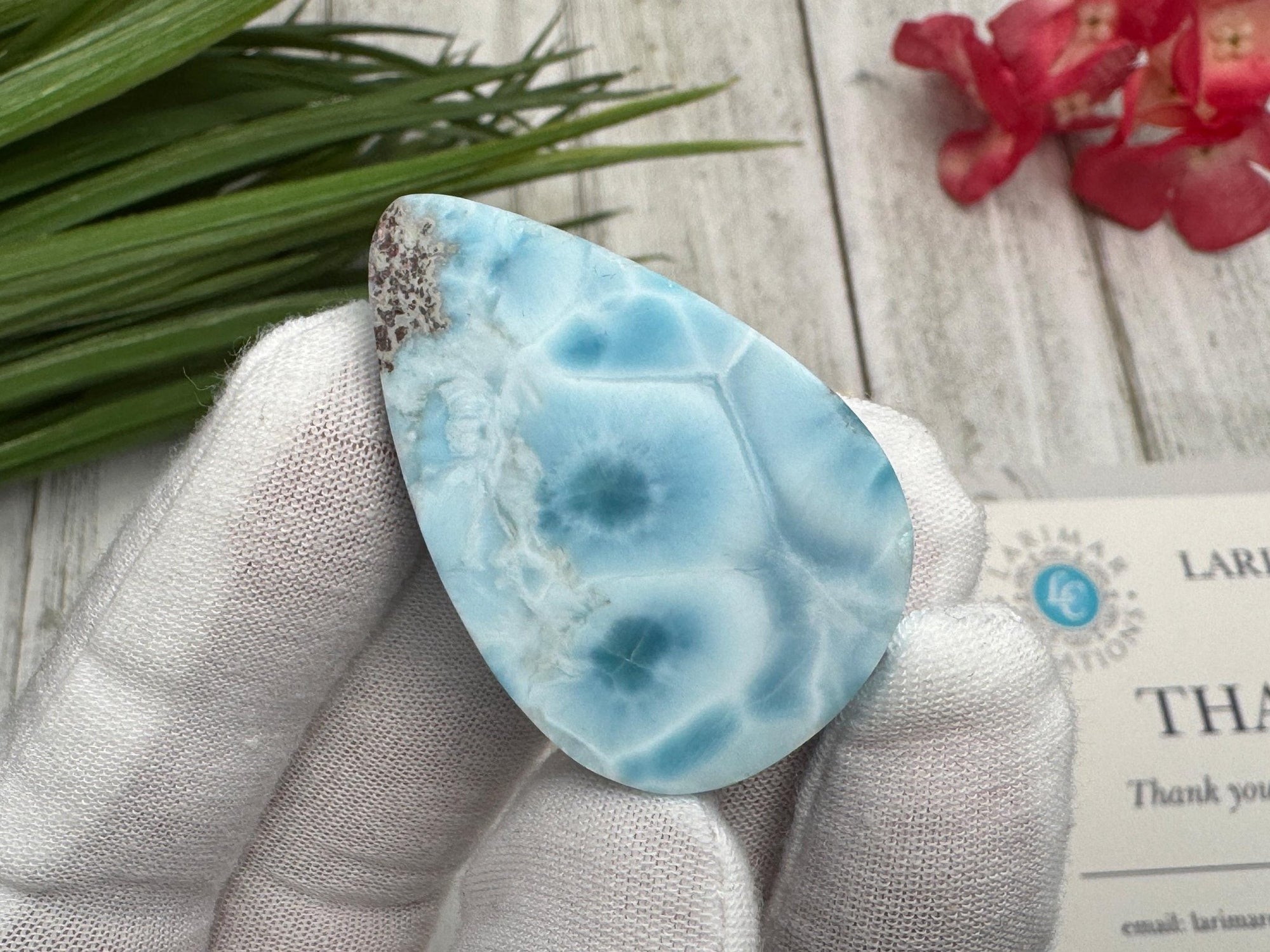 High-quality blue Larimar gemstone with ocean-like patterns, displayed in a white-gloved hand next to a branded