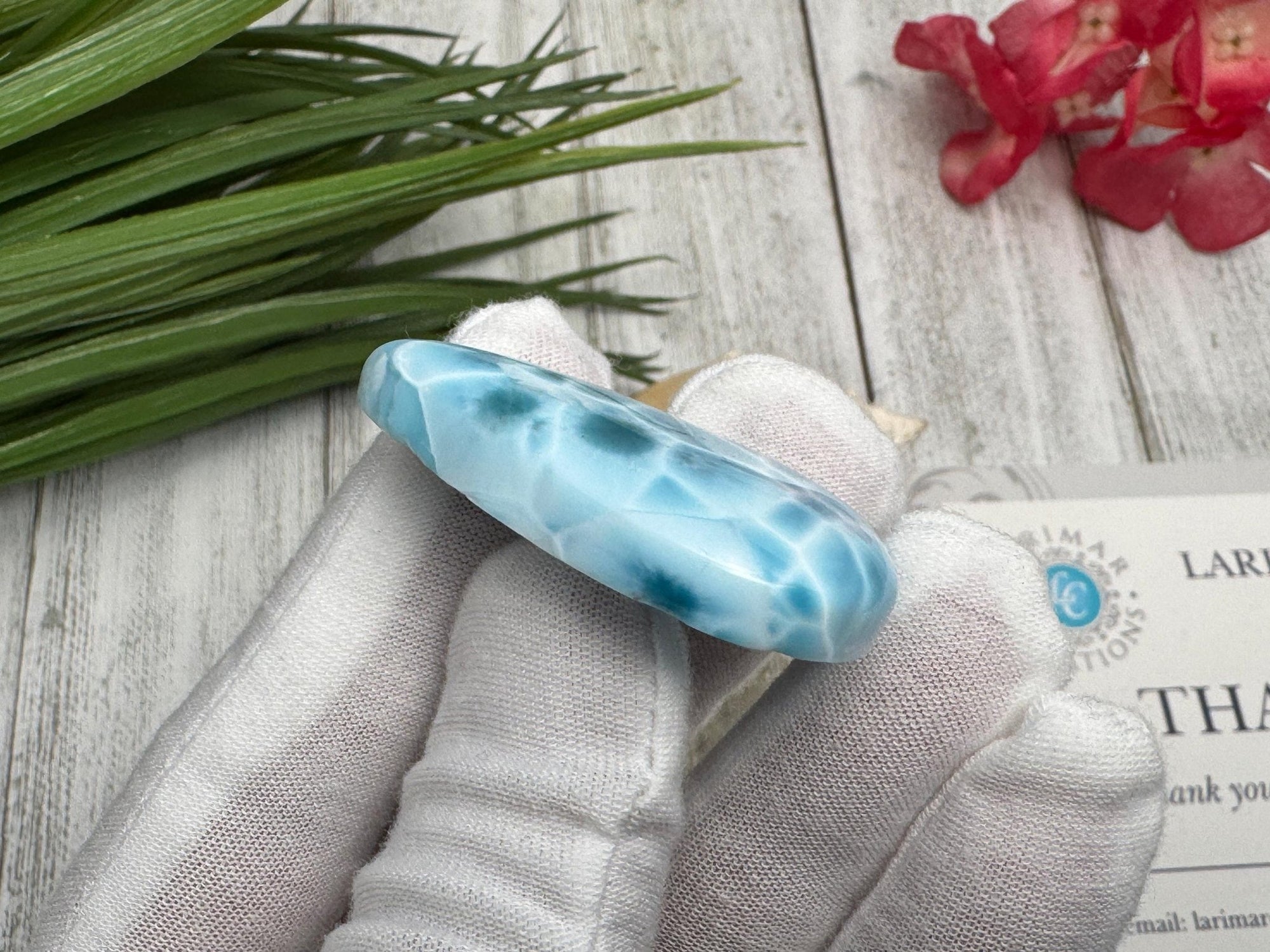 High-quality blue Larimar gemstone with ocean-like patterns, displayed in a white-gloved hand next to a branded