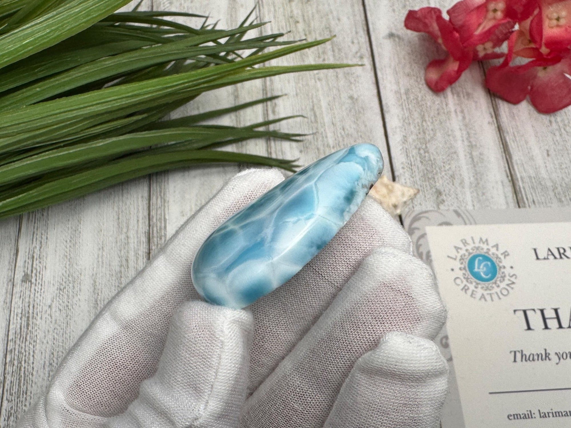 High-quality blue Larimar gemstone with ocean-like patterns, displayed in a white-gloved hand next to a branded