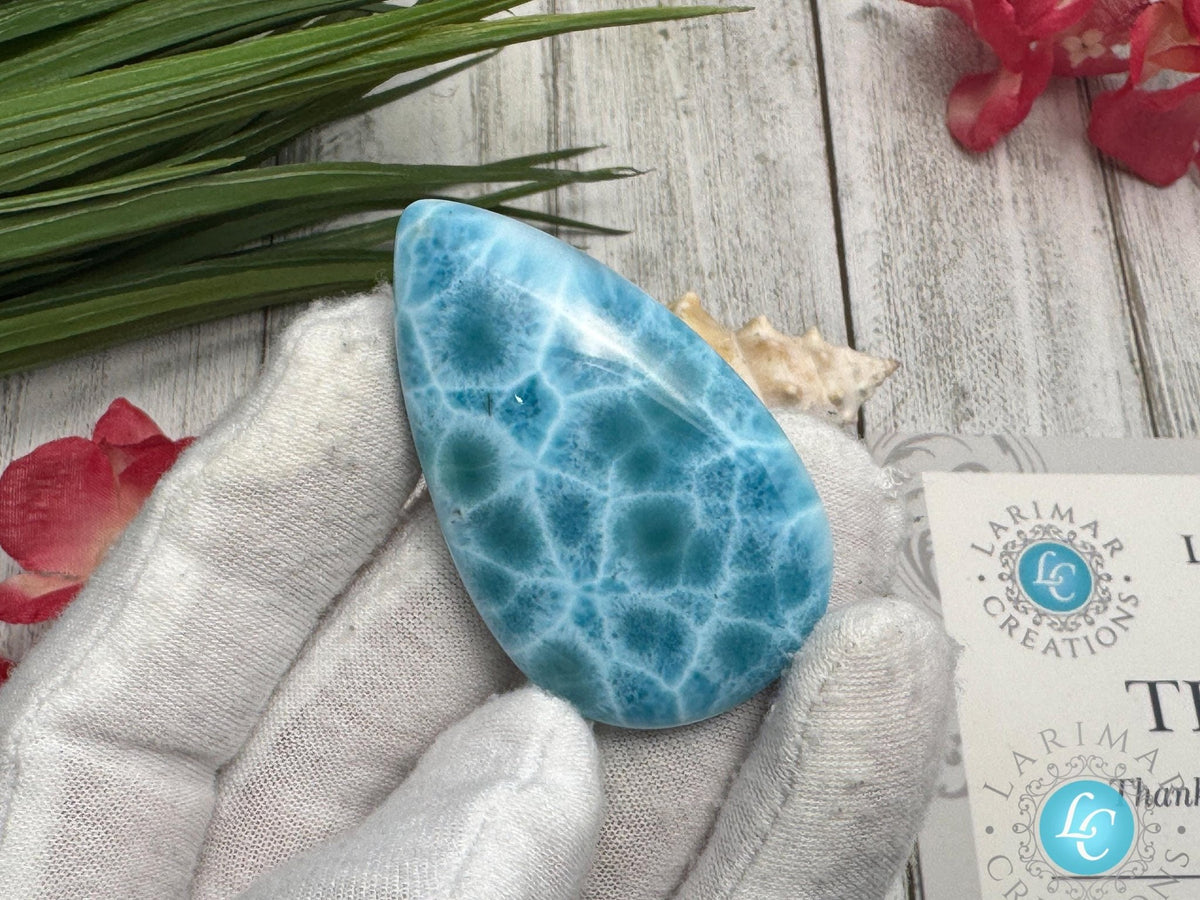 Close-up of a high-quality Larimar cabochon with vibrant Caribbean blue hues and natural white patterns, polished