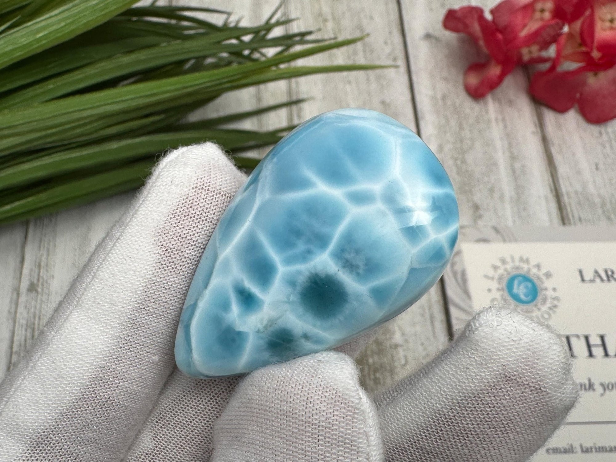High-quality blue Larimar gemstone with ocean-like patterns, displayed in a white-gloved hand next to a branded