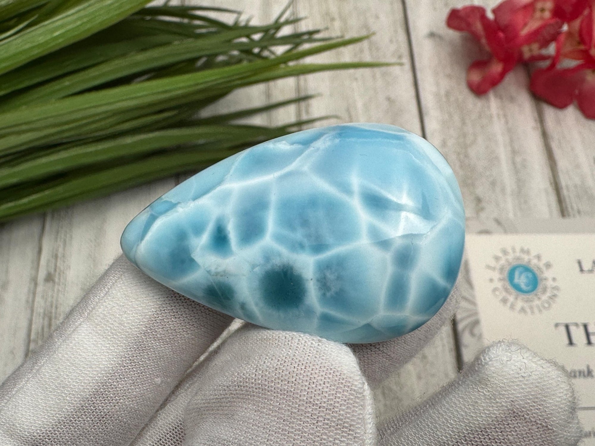 High-quality blue Larimar gemstone with ocean-like patterns, displayed in a white-gloved hand next to a branded