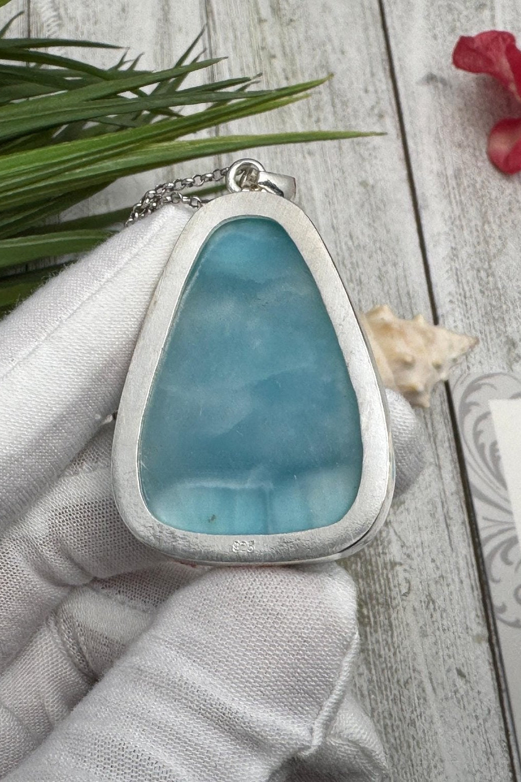 Handcrafted Larimar pendant necklace featuring a natural blue gemstone, held in a white-gloved hand against a rustic