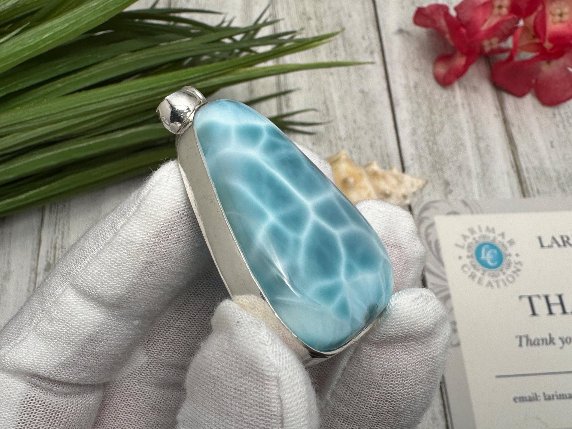 Close-up of a polished Larimar pendant set in sterling silver, held in a gloved hand against a wooden background with