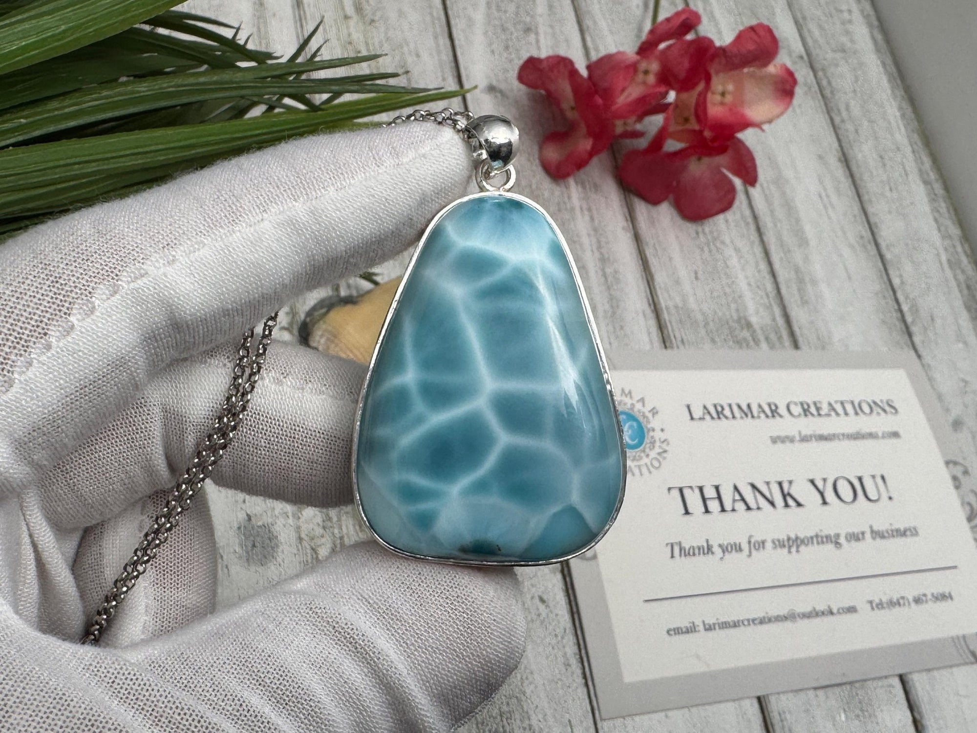 Close-up of a polished Larimar pendant set in sterling silver, held in a gloved hand against a wooden background with