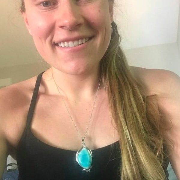 Woman wearing a black tank top with a turquoise pendant necklace indoors.