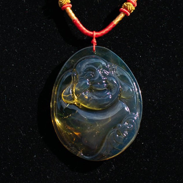 Blue amber pendant BUDDH Aon a red cord against a black background