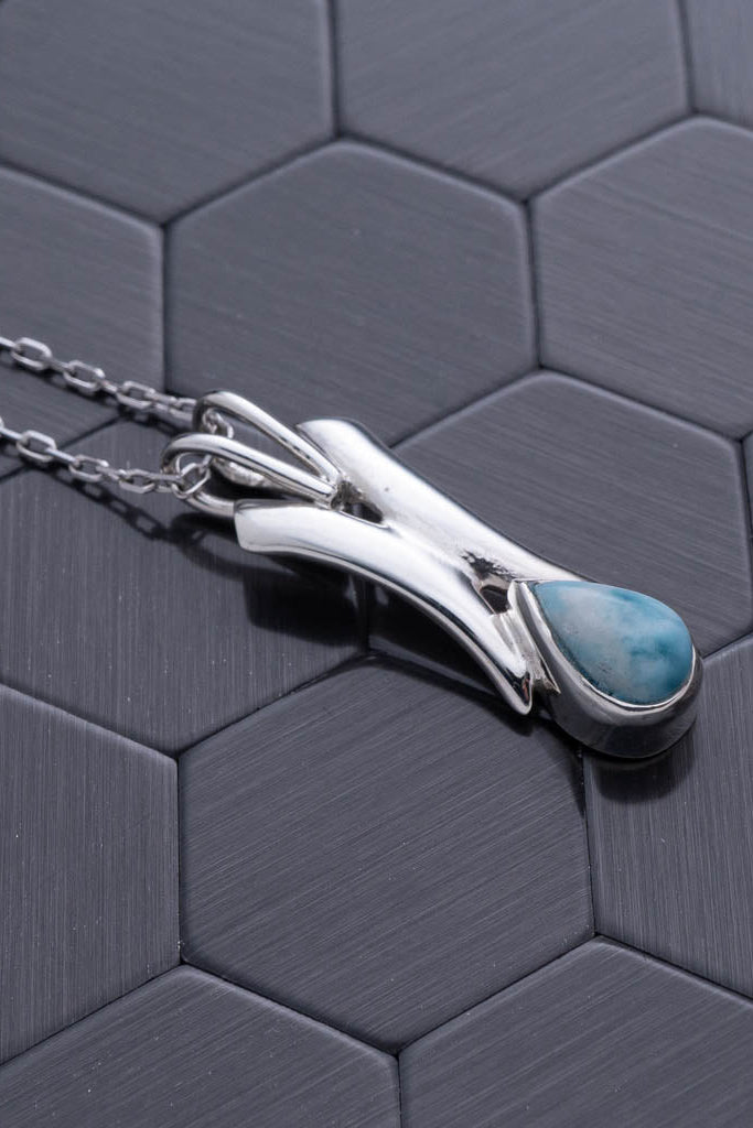 Silver necklace with a blue stone pendant on a hexagonal patterned surface