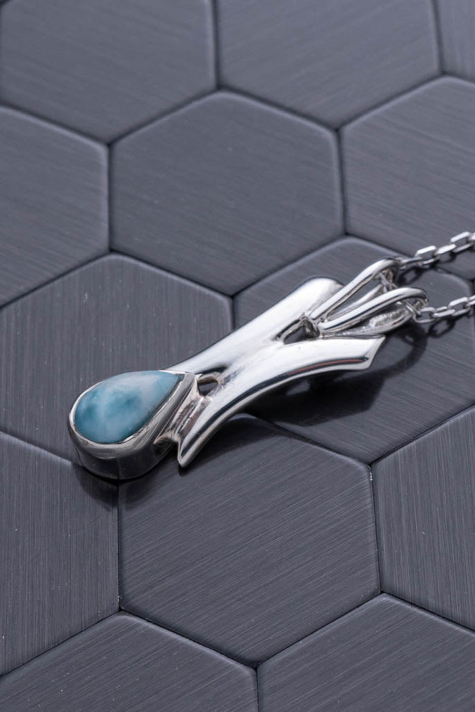 Silver pendant with a blue stone on a hexagonal patterned surface