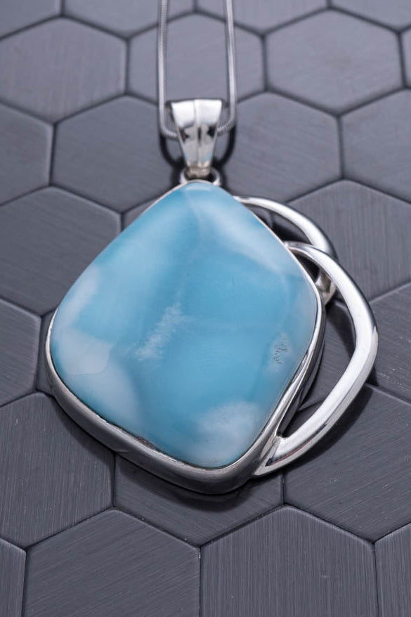 Turquoise pendant with silver frame on a hexagonal patterned surface