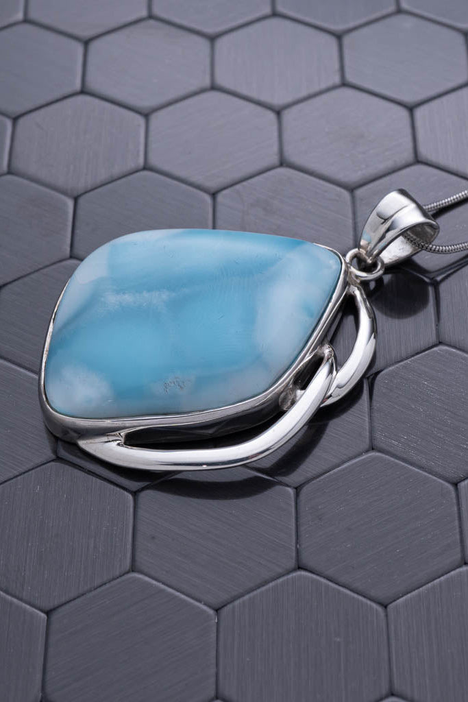 Turquoise stone pendant on a silver chain against a hexagonal patterned background