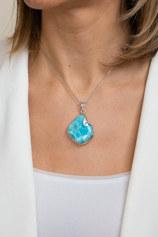 Woman wearing a necklace with a blue pendant against a neutral background