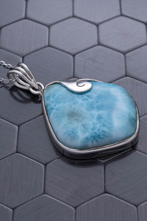 Blue stone pendant on a silver chain against a hexagonal patterned background