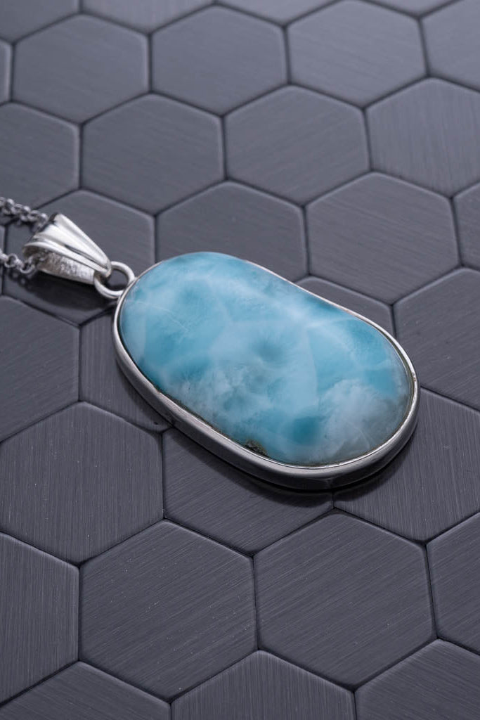 Turquoise stone pendant on a silver chain against a hexagonal patterned background