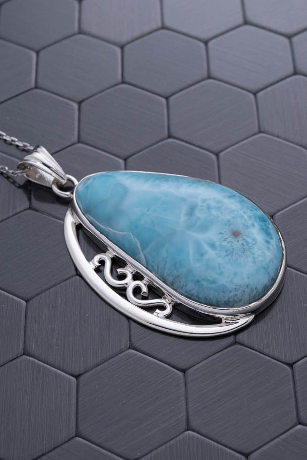 Silver pendant with a blue stone on a hexagonal patterned surface