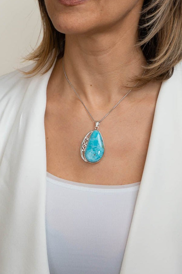 Woman wearing a necklace with a blue pendant against a neutral background
