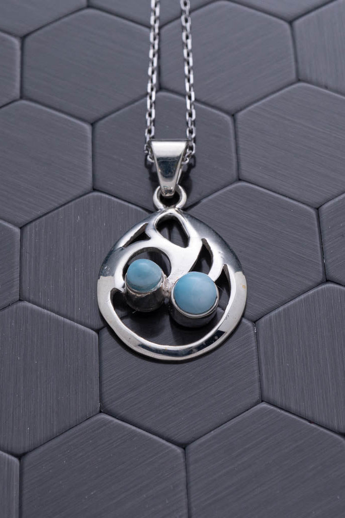 Silver necklace with a circular pendant featuring two blue stones on a hexagonal patterned surface.