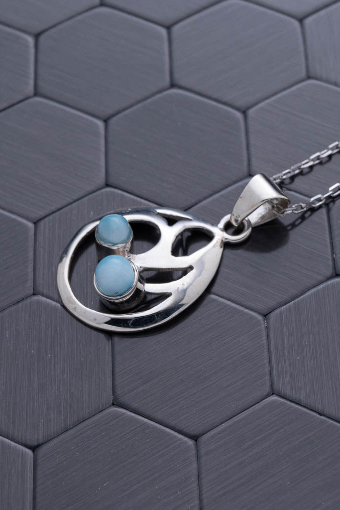 Silver necklace with a paw-shaped pendant featuring blue stones on a hexagonal patterned surface.
