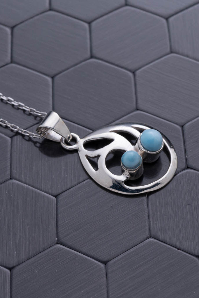 Silver necklace with a pendant featuring turquoise stones on a hexagonal gray surface